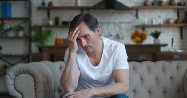 Беспокойный зрелый мужчина, страдающий депрессией, сидит дома на диване — стоковое видео