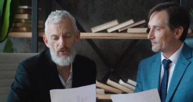 Masada otururken modern ofiste iş büyümesini tartışan iki yetişkin iş adamı. İçerde buluşurken iş arkadaşınla anlaşma hakkında konuşan bir adam.