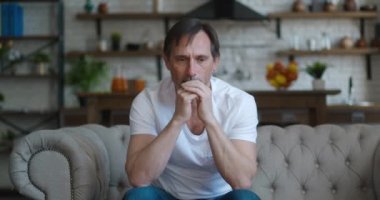 Depresyondan muzdarip üzgün olgun bir adam, evdeki kanepede oturuyor. Oturma odasında kanepede otururken ruhsal sorunları olan üzgün bir erkek..