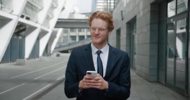 Gözlüklü ve resmi takım elbiseli kızıl saçlı işadamı şehir merkezindeki caddede akıllı telefon mesajları, gülen yüz teknolojisi iletişimi kullanıyor.