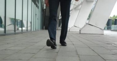 Siyah ayakkabılı iş adamlarının ayakları ve resmi kıyafetleri ön planda, dışarıda yürüyor, adımlar atıyor, işe gidip geliyor, düzenli çekim yapıyor..