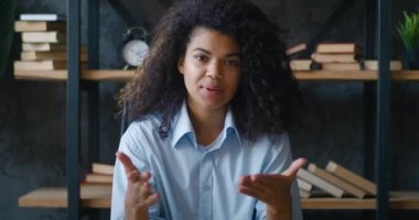 POV webcam görüntüsü, gülümseyen Afro-Amerikan iş kadını kamerayla konuşuyor, ofisten çevrimiçi video görüşmesi yapıyor. Dijital blogger vlogger talk show ev ofis stüdyosunda, masa başında oturuyor.