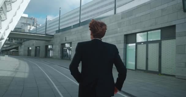 Back view red-headed businessman running through downtown to get to his office on time. Young man entrepreneur is late for meeting at work. Rear view male manager in hurry to appointment. Slow motion — стоковое видео