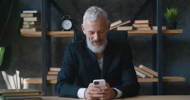 Excited mature business man hold smartphone overjoyed male winner celebrate mobile online bid game win victory success receive read good news on cellphone while sitting at modern office — Stock videók