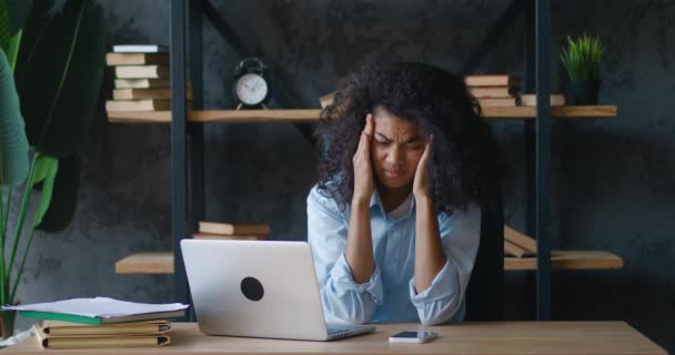 Gestresste junge Geschäftsfrau, die unter Überarbeitungskopfschmerzen leidet, wenn sie am Computer sitzt, während sie am Tisch im Büro sitzt. Gelangweilte afrikanisch-amerikanische Studentin hat genug von der Arbeit am Laptop — Stockvideo