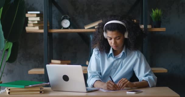 African woman student writing notes from laptop. Girl in headset distant learning on quarantine isolated. University female studying online concentated. Education concept — Video Stock