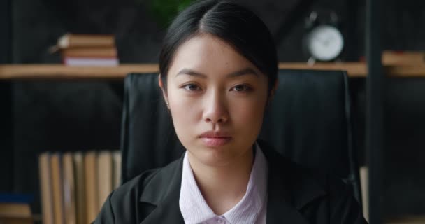 Крупный план портрета уверенной молодой брюнетки азиатской бизнес-леди, офисного менеджера или студентки, в формальном костюме, смотрящей в камеру на офисном фоне — стоковое видео