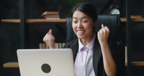 Overjoyed asiático jovem mulher de negócios trabalhando no computador portátil no escritório. Trabalhadora de escritório excitada olhando para tela do monitor lendo ótimas notícias e está encantada. Mostrando sim gesto — Vídeo de Stock