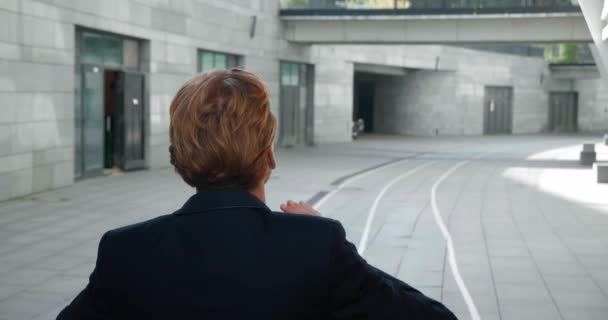 Back view of caucasian red-haired businessman walking outdoors the street at downtown. Rear view of male employee wearing classical suit going to work — Wideo stockowe