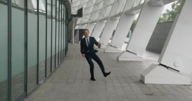 Şaşırtıcı iş adamı zaferle sevinir, havaya atlar ve evet işaretini gösterir. Heyecanlı erkek işadamı, modern ofis binasının yakınında dikilirken zaferi kutluyor.