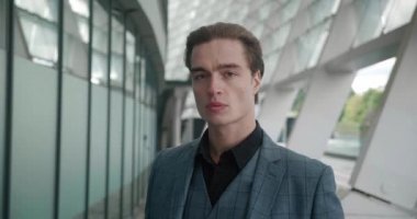 Modern ofis binasının yakınında dikilip kameraya bakan takım elbiseli, kendine güvenen yakışıklı iş adamlarının yakın çekimi. Açık havada hırslı bir yönetici portresi.