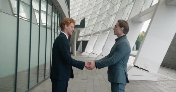 Business partners shaking hands outdoors. Two businessmen in formal suits, shake hands with each outside other near office building, agree to deal or say hello — стоковое видео