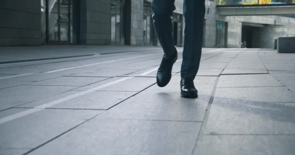 İşe gidip gelen bir iş adamının önü. Kendine güvenen deri ayakkabılı ve resmi takım elbiseli bir adam şehir merkezinde ofis binasının yanında yürüyor.. — Stok video
