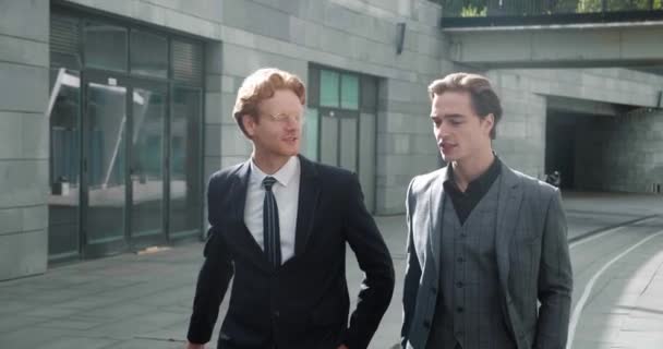 Two caucasian business partners in formal clothes having conversation outdoors while walking at downtown. Concept of business people, cooperation and success. — Video