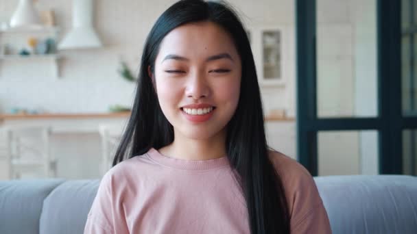 Porträt einer selbstbewussten, schönen jungen Asiatin, die zu Hause auf der Couch sitzt. Charmante junge asiatische Ethnizität Frau lächelt mit zahmem Lächeln, blickt zuversichtlich in die Kamera, sitzt auf dem Sofa zu Hause — Stockvideo
