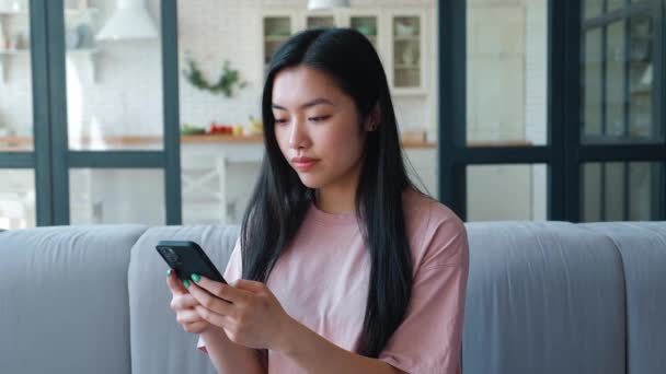 Confident portrait of a serene dark-haired Asian woman using her smartphone for texting, browsing mobile apps, shopping and booking. The place of digital electronic devices in everyday life — Stockvideo