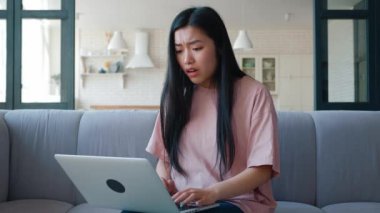 Main focus on negative emotions of Asian woman. Student, freelancer is disappointed, after being seen on the screen of monitors, in frustrated feelings, closes the laptop lid with tears in her eyes