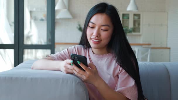 Front view of a serene happy dark-haired Asian woman using her smartphone for texting, browsing mobile apps, swipping, shopping and booking. The place of digital electronic devices in everyday life — Stockvideo