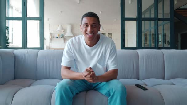 An excited and agitated young African American nervously watches the match on TV, applauds, rejoices at the victory of the team he is rooting for. Mixed race man relaxing at home and watching tv — Vídeo de Stock