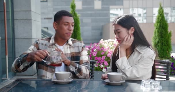 Όμορφος Αφροαμερικανός κάθεται στο τραπέζι στο lounge cafe με την κοπέλα του, ρίχνει ζεστό τσάι σε φλιτζάνια και ξοδεύει πολύτιμες ρομαντικές στιγμές με την κοπέλα του ενώ μιλάει μαζί — Αρχείο Βίντεο