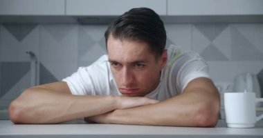 Evdeki masada oturan endişeli ve stresli genç adamın portresi. Depresyondaki erkek keder ya da başarısızlıktan muzdarip