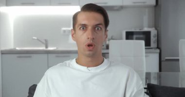 Başarıyı kutlayan, kameraya şaşıran, evdeki oturma odasındaki kanepede oturan genç adamın yakınlaşması. Zafer konsepti. Evet kazanan jest.