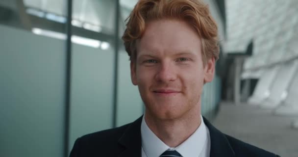 Cheerful young redhead businessman looking at the camera and while standing in the business district near the office building. Close-up portrait — Stockvideo