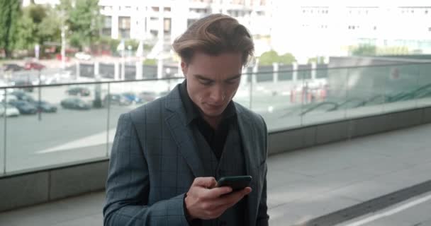 Confident male entrepreneur uses mobile phone e-commerce app for stock market investment. Stylish businessman using smartphone standing outdoors on street of business district in downtown — Stock videók