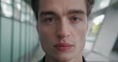 Close-up portrait of ambitious businessman standing outdoors. Macro face of confident young man entrepreneur looking at camera outside near modern office building