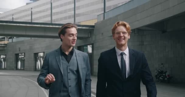 Steadicam shot of two men business professionals in formal suits walking together down street and talking. Two caucasian business partners having conversation outdoors while walking at downtown — Vídeo de Stock