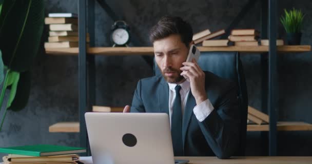 专注于在现代办公室笔记本电脑上工作的留胡子商人 男性员工在使用电脑的时候 在电话中接听专业人员的电话 — 图库视频影像