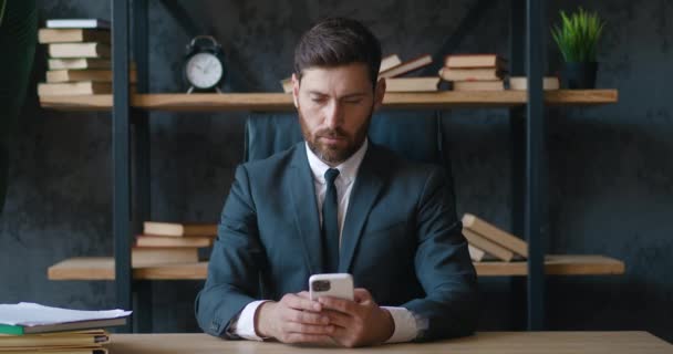 留胡子的商人手持现代智能手机 在办公室发短信 年轻男性员工使用现代手机技术商业应用 在办公桌前输入电子邮件 — 图库视频影像