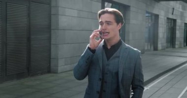 Resmi takım elbiseli ciddi bir erkek işadamı cep telefonuyla konuşuyor şehir merkezindeki ofis binalarının yakınında ağır çekimde yürürken bir iş anlaşmasını tartışıyorlar.