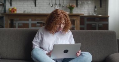 Üzgün genç bir kadın evdeki kanepede otururken dizüstü bilgisayarında kötü mesajlar okuyor. Mutsuz, depresyondaki genç bir kadın bilgisayar ekranına bakıyor. İnternet bahis kaybı tepkisi.