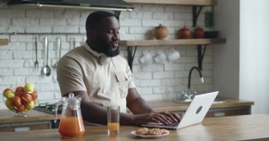 Afrikalı girişimci, evde mutfaktayken bilgisayarını uzaktan kumandalı online video görüşmesi için kullanır. Evde video konferansı yapan serbest çalışan bir adam..