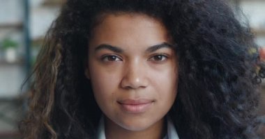 Güzel, gülümseyen, kıvırcık saçlı Afro-Amerikan kadın kameraya bakıyor. Ofiste poz veren mutlu ve çekici bir kadın. Yüz portresini kapat