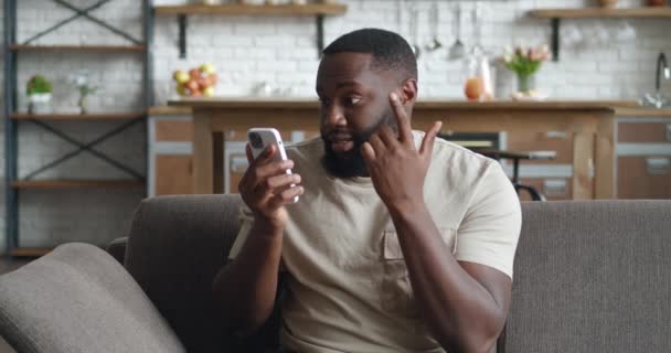 Африканський чоловік розстроюється, коли розмовляє по мобільному у себе вдома. Гнів діловий чоловік кричить під час телефонного дзвінка сидячи на дивані у вітальні. — стокове відео