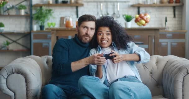 Un hombre le enseña a su novia a jugar un videojuego mientras está sentado en el sofá de su casa. La pareja se pelea y comparte el joystick mientras juega a la consola de juegos durante el tiempo libre en casa. — Vídeos de Stock