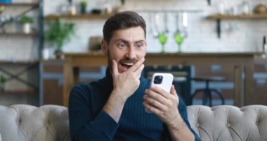 Heyecanlı ve hoş bir şekilde şaşırmış yakışıklı adam akıllı telefonundaki mesajla seviniyor. Genç bir erkek cep telefonuna bakıyor ve şaşkına dönmüş ve arka planda 