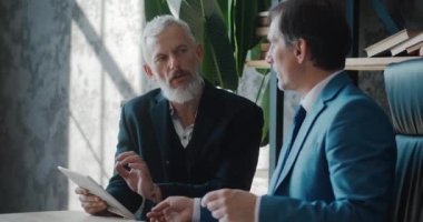 Masada otururken modern ofiste iş büyümesini tartışan iki yetişkin iş adamı. İçerde buluşurken iş arkadaşınla anlaşma hakkında konuşan bir adam.