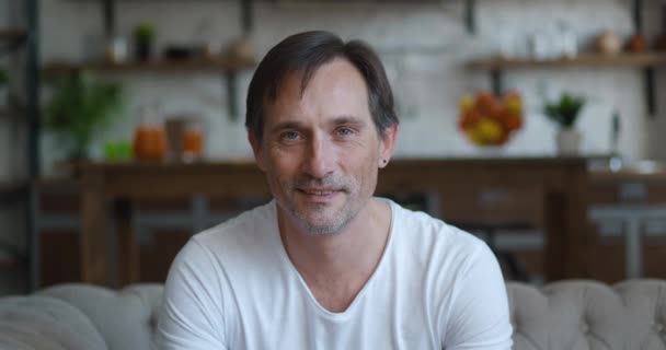 Close-up portrait of successful caucasian mature man smiling looking at camera while sitting at home on sofa. Headshot of senior male on kitchen background — Vídeo de Stock