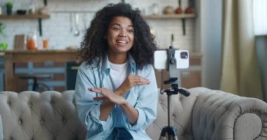 Genç Afrikalı Amerikalı kadın blogger vlogger video kaydediyor ya da akıllı telefondan canlı yayında evdeki kanepede otururken. Bloglama ve video yayınları kavramı.