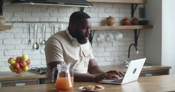Emozionato imprenditore africano vincitore con laptop in cucina. Felice studente uomo gesticolando sì gesto guardando computer portatile in eccitazione dopo aver vinto la lotteria mentre seduto a tavola in cucina a casa — Video Stock