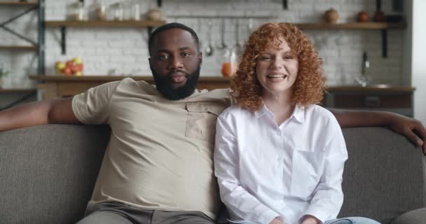 Retrato de pareja interracial sentados en un sofá juntos y mirando a la cámara posando en el fondo de la cocina de su apartamento en casa — Vídeos de Stock