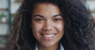 Neşeli Afro-Amerikalı kadın kameraya bakıp diş tebessümüyle gülüyor. Güzel, gülümseyen genç bir bayan. 20 güzel yüz kameraya bakıyor. Evde tek başına poz veriyor.