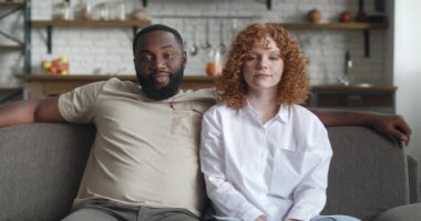 Aynı koltukta oturan ve evlerinin mutfak arka planında poz veren iki farklı ırktan çiftin portresi