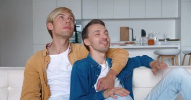 Mutlu erkek homoseksüel çift evlerinde kanepede kucaklaşarak oturuyor. Erkek eşcinsel çift evde vakit geçiriyor. LGBT İlişkisi