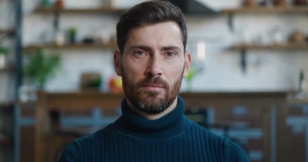 Retrato de cerca del exitoso hombre caucásico sonriendo mirando a la cámara mientras está sentado en casa en el sofá. Cabeza de hombre barbudo sobre fondo de cocina — Vídeo de stock