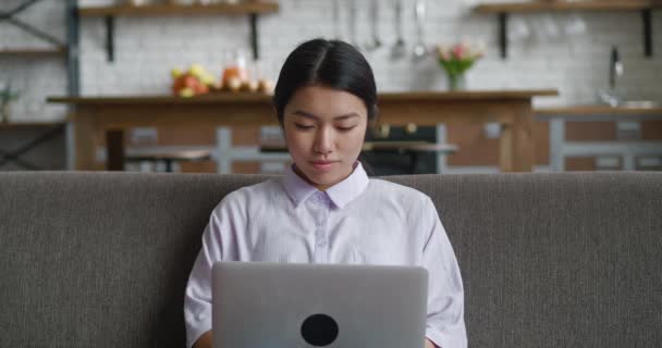 Mujer asiática descansando en el sofá usando portátil portátil mirando el mensaje de escritura de pantalla en la sala de estar, mujer joven charlando en la computadora navegando por Internet redes sociales estudiando o trabajando en línea en casa — Vídeos de Stock