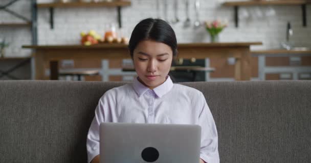 Asijské žena odpočívá na gauči pomocí notebooku při pohledu na obrazovce psaní zprávy v obývacím pokoji, mladá žena chatování na počítači procházení internetu sociální média studium nebo práci on-line doma